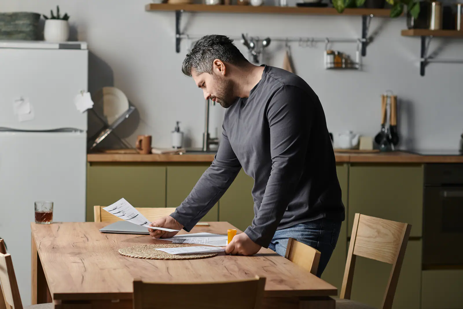 A man standing at a kitchen table reading through papers before deciding what to do with his car