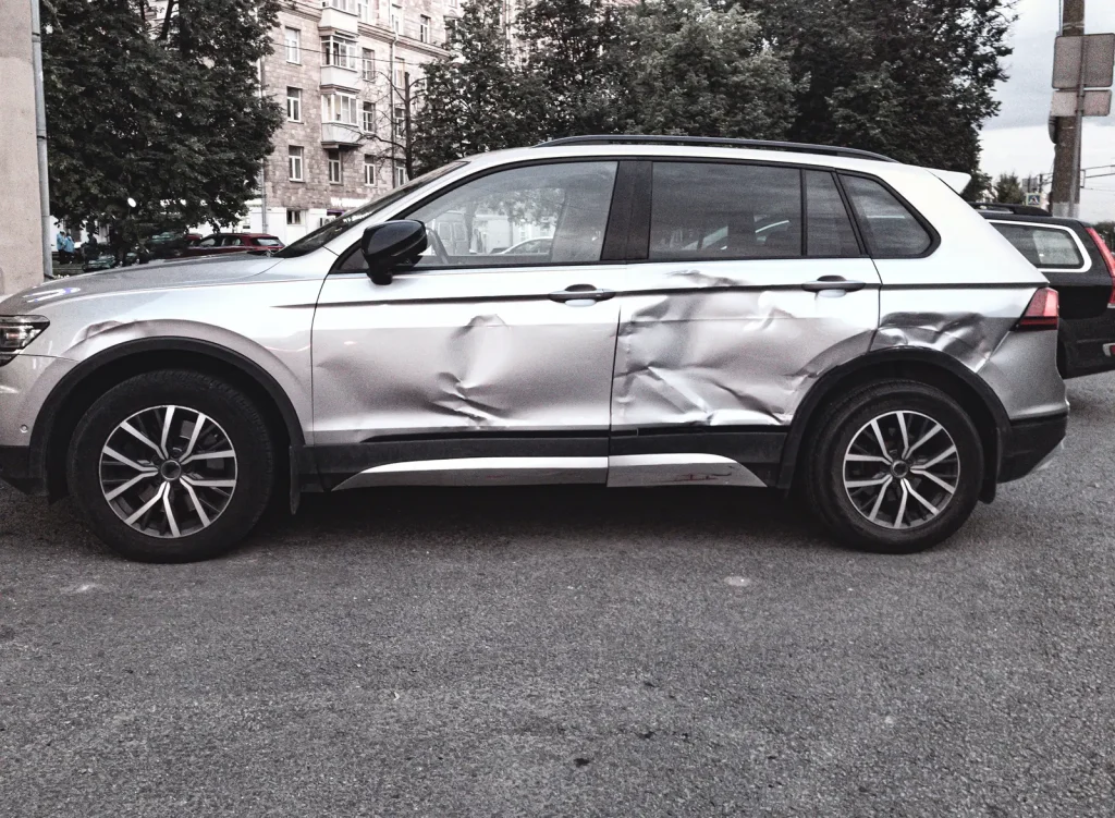 A silver SUV parked on a street with both doors on one side badly dented